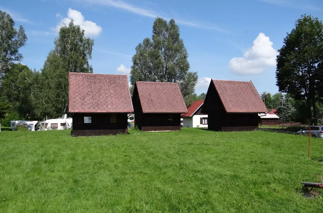 Tři dřevěné chaty na autokampu v Hejnicích pod modrou oblohou.