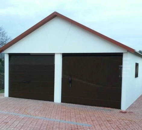 Bílá omítnutá garáž s dvěma tmavými brány na dlažbě.