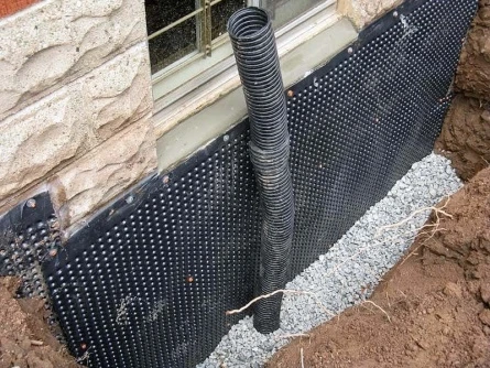 Instalace černé nopové folie u základu domu s kamenivem.