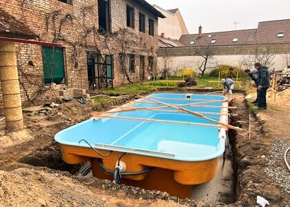 Modrý nadzemní bazén se instaluje v jámě vedle staré budovy.