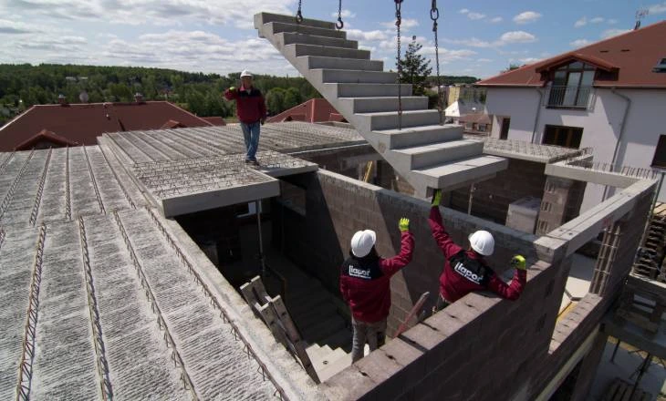 Montáž betonového schodiště na střeše budovy s dělníky.