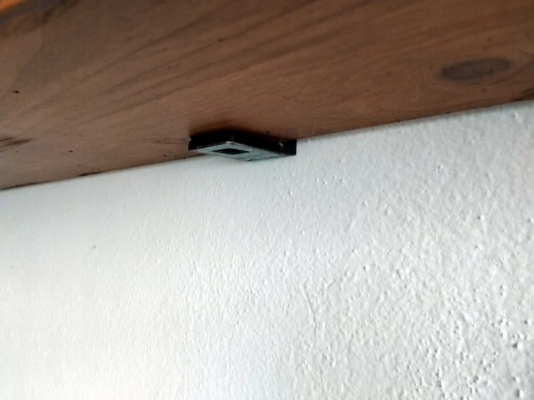 Kuchyňská polička namontovaná na zdi pomocí kovového držáku.
