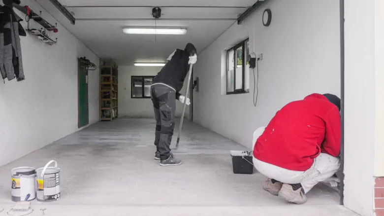 Dva lidé malují betonovou podlahu v garáži.