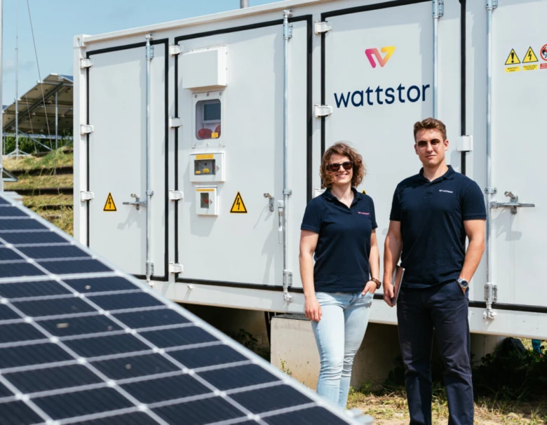 Dva lidé stojí před velkou bateriovou jednotkou s fotovoltaickými panely.