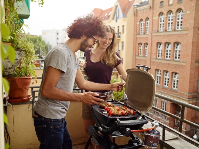 Muž a žena grilují na plynovém grilu na balkóně.