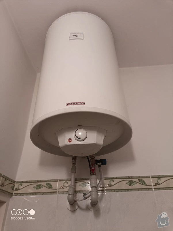Bílý bojler značky Stiebel Eltron s připojenými hadicemi v koupelně.