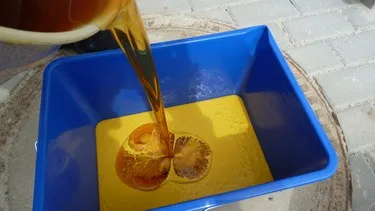 Nalévání tekutého nátěru do modrého kontejneru pro úpravu podlahy v garáži.