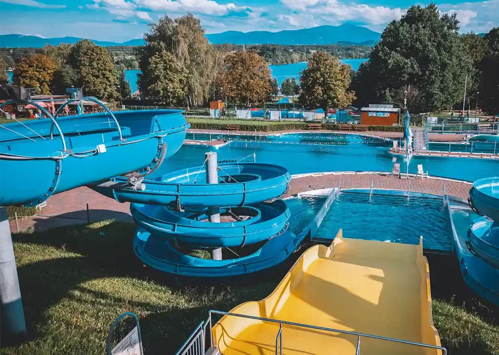 Modré vodní skluzavky v bazénu aquaparku Olešná s horami na pozadí.