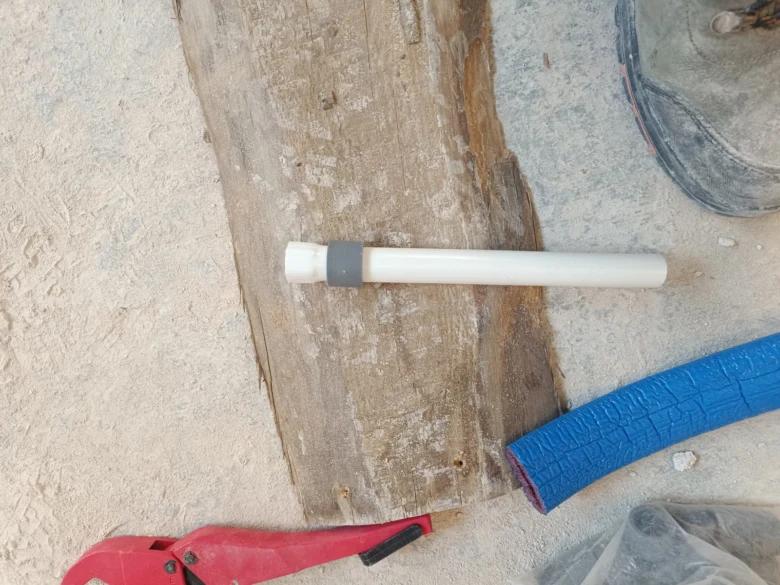 Bílá plastová trubka s nástavcem leží na zemi vedle řezačky.