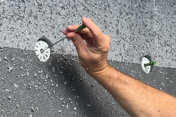 Ruční instalace kotvy do desky z expandovaného polystyrénu na fasádě.