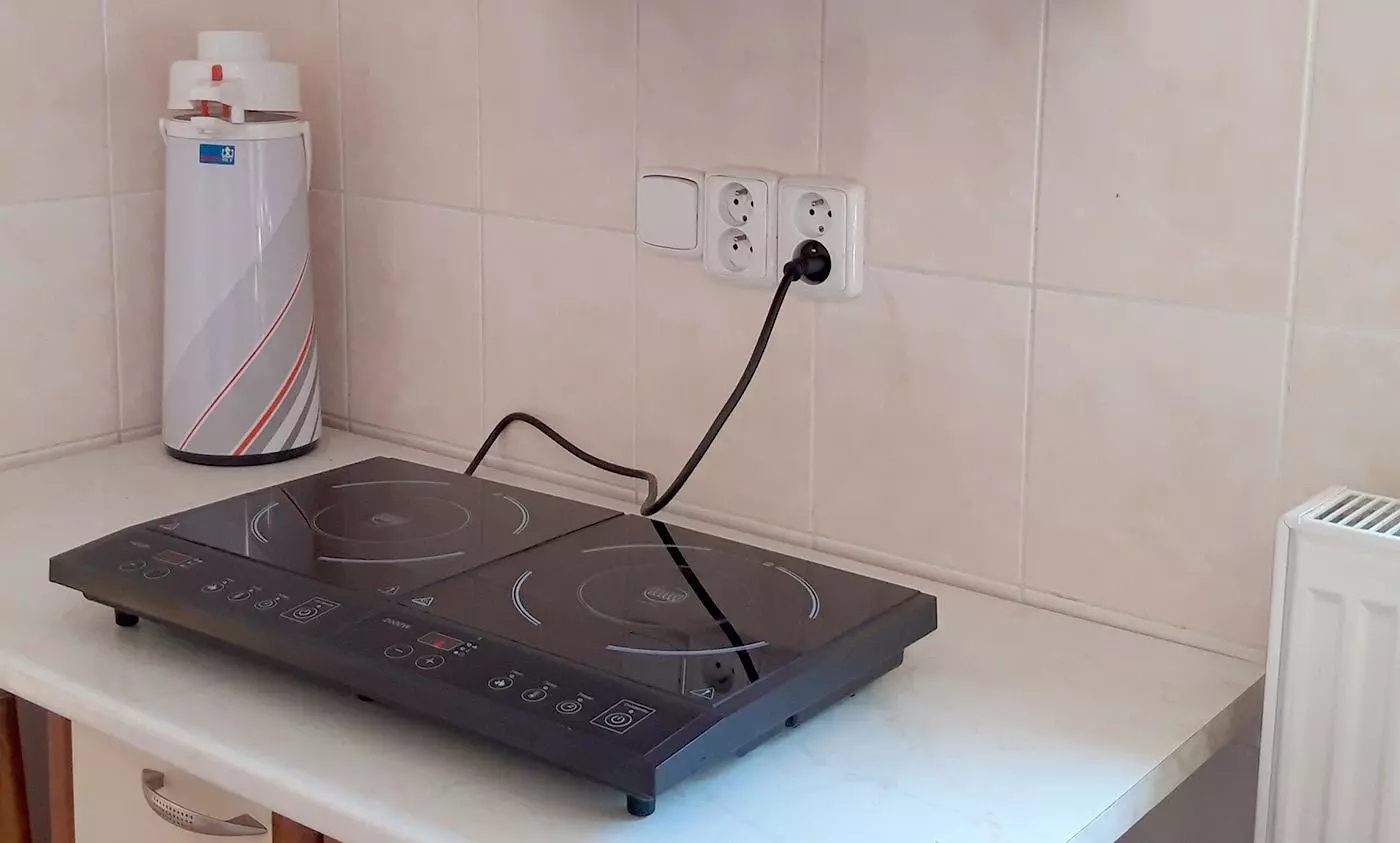 Indukční varná deska zapojená do zásuvky na kuchyňské pracovní ploše.