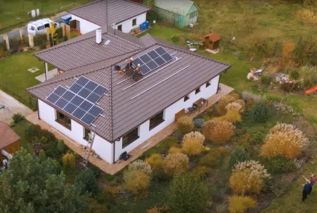 Dva dělníci montují fotovoltaické panely na střechu rodinného domu.