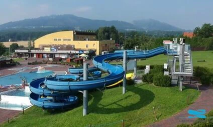 Modré vodní skluzavky vedle bazénu v koupališti s horami na pozadí.