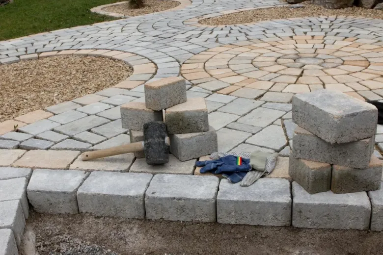 Sedí betonové dlaždice s kladivem rukavicemi pro instalaci.