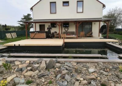 Dřevěná terasa ve svahu s vodním prvkem u domu.