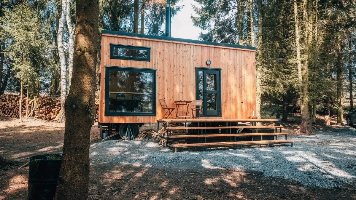 Hotový dům typu tiny house uprostřed lesa s venkovním posezením.