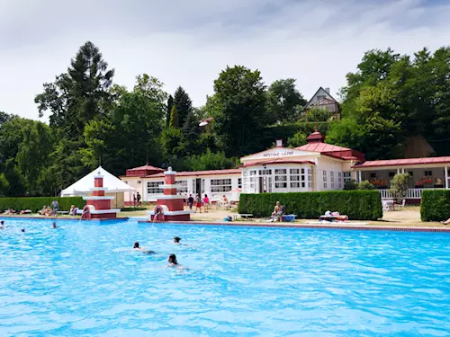 Venkovní bazén s lidmi a budovami v okolí koupaliště.