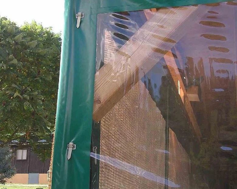 Detailní pohled na průhlednou plachtu připevněnou k zelenému rámu pergoły.