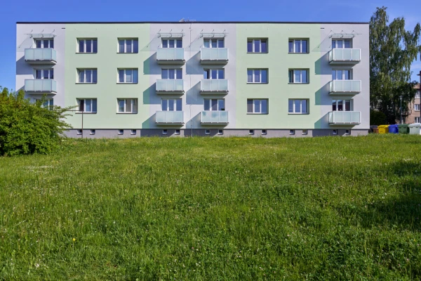 Zateplený bytový dům s balkony na pozadí zelené trávy.