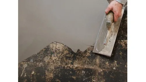Ruka rozšiřuje samonivelační stěrku na nerovný podlahový povrch.