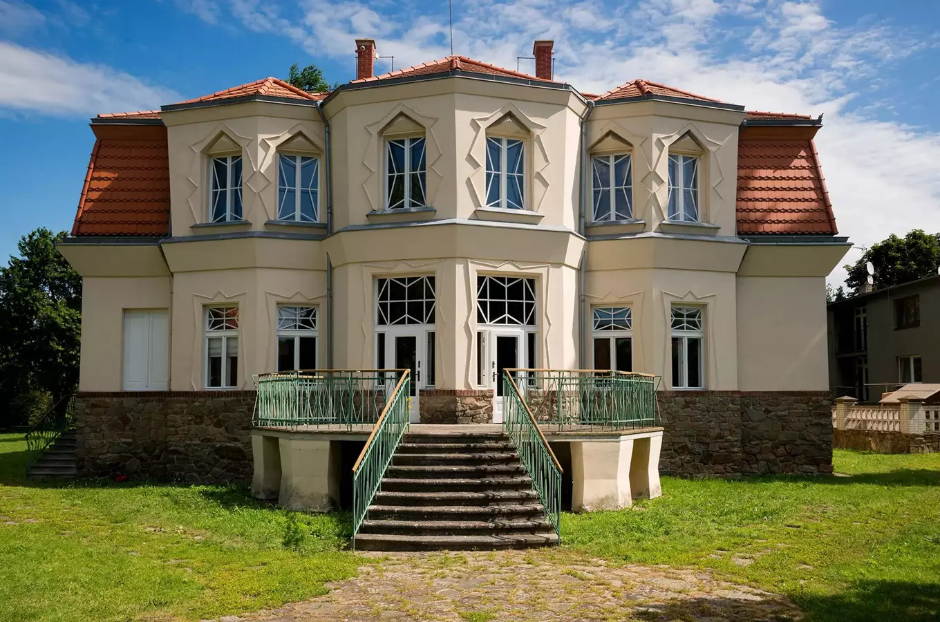 Fasáda kubistického domu s geometrickými okny a kamenným základem.