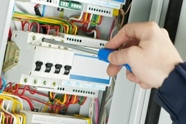 Elektrikář upravuje komponenty v rozvaděči šroubovákem.