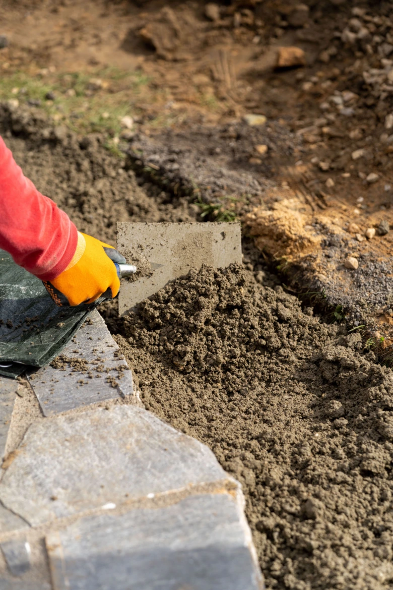 Ruční aplikace betonu mezi kameny při stavbě zdi.