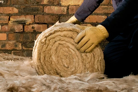 Pracovník s rukavicemi rozbaluje válec minerální vaty před zateplením fasády.