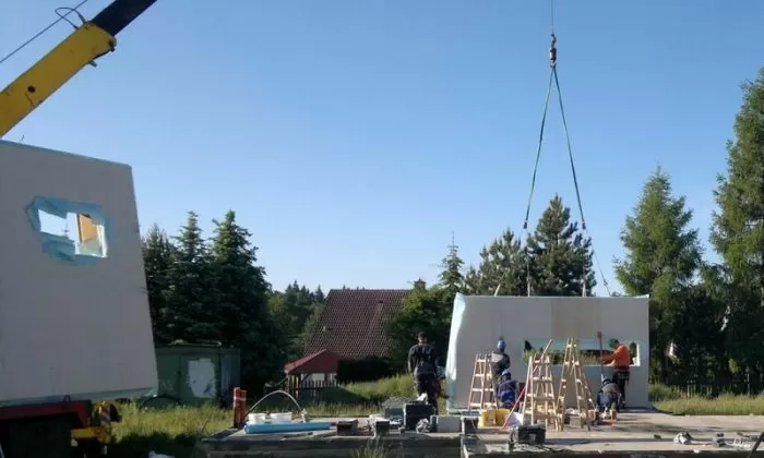 Stavba dřevěné chaty s montáží prefabrikovaného modulu na místě.