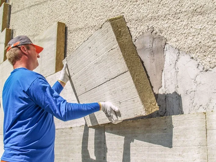 Muž montuje minerální vatu na fasádu při zateplování.