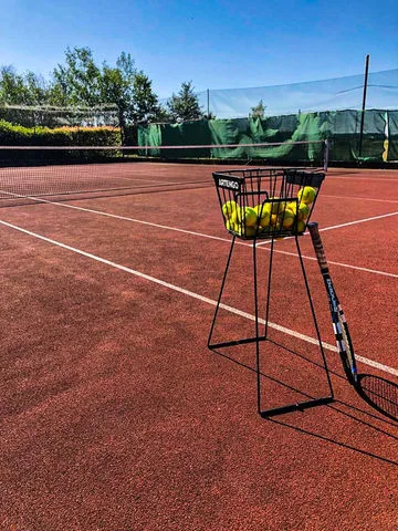 Tennis dvorec s košíkem míčů a rakety na červeném povrchu.