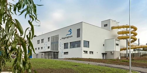 Bílá budova Aquacentra s žlutou vodní skluzavkou na Moravě.