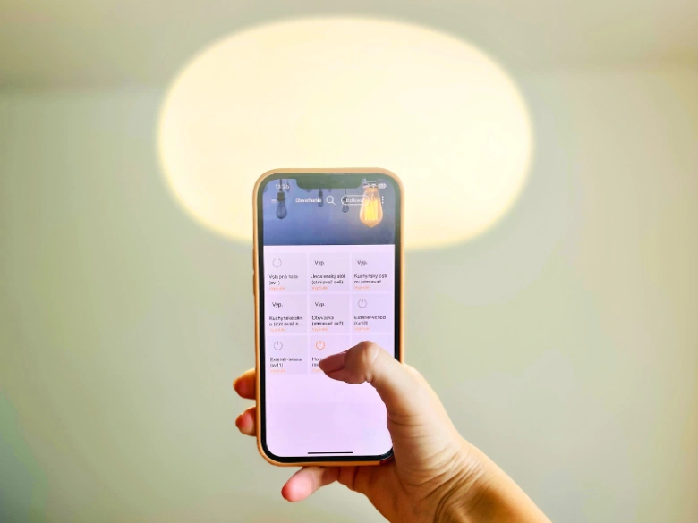 Ruka drží chytrý telefon s aplikací pro řízení osvětlení.