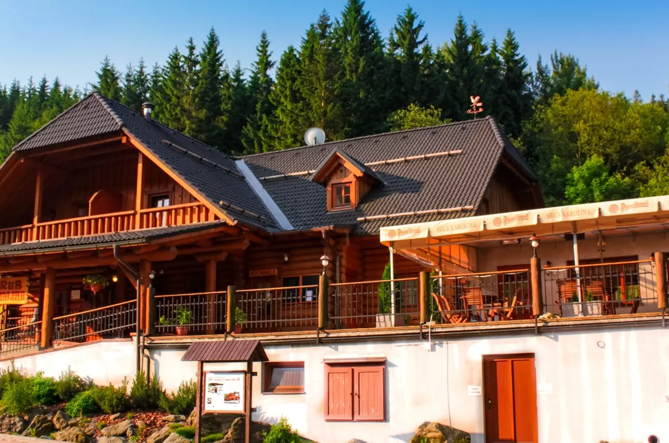 Dřevěný srub s terasou a venkovním posezením pod plachtami.