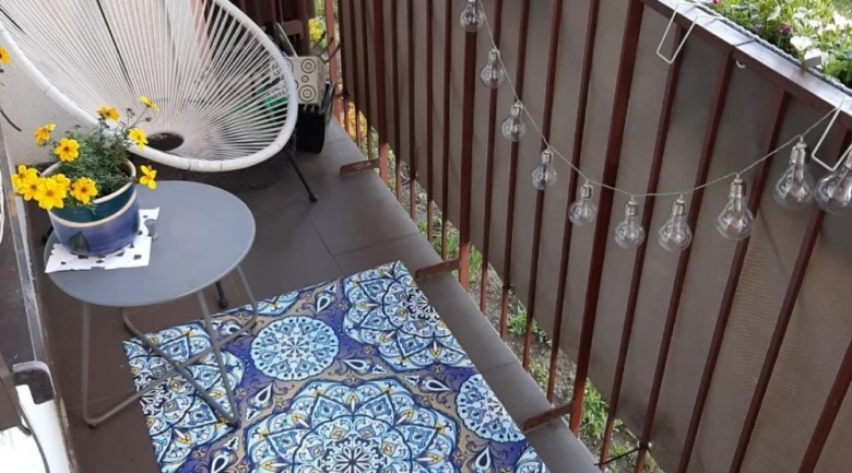 Balkon s modrou dlažbou, židlí a květinami.