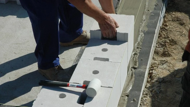 Stavebník položí betonové bloky na základovou vrstvu.