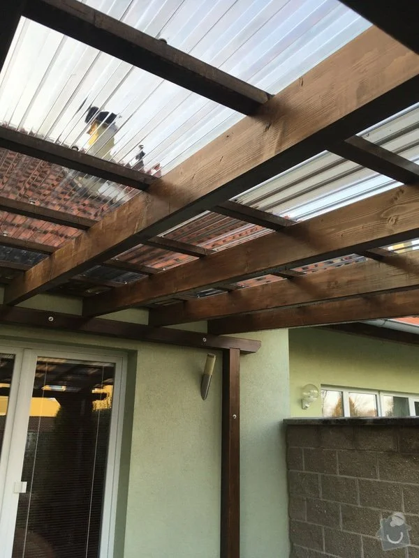 Stavba moderní dřevěné pergoly u domu s průsvitným střešním materiálem.