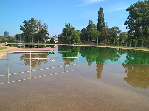 Přírodní koupaliště s odrazem stromů v klidné vodě.