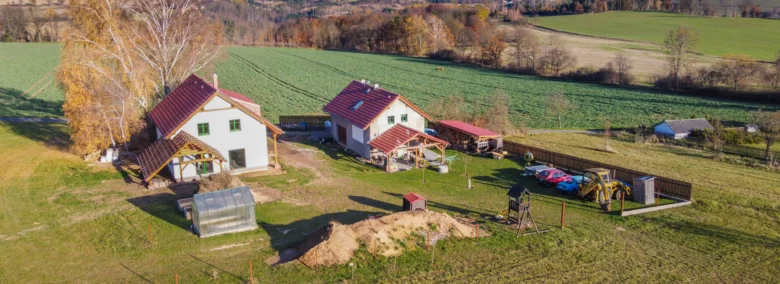 Dvě venkovské domky na pozemku s poli bez viditelných rekuperačních systémů.
