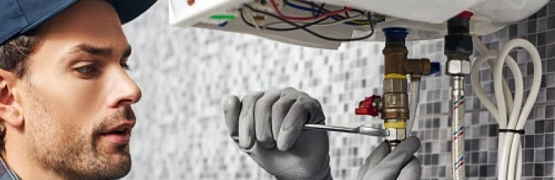 Montér opravuje bojler pomocí klíče pod odhaleným elektrickým ohřívačem vody.