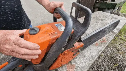 Oranžová motorová pila s řetězem na dřevěné desce.