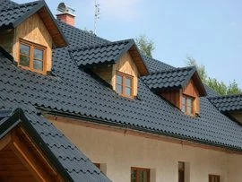 Fotografie tmavých plechových tašek na střeše domu s vikýři.