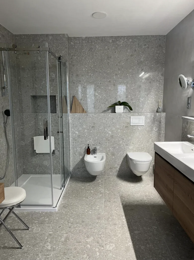 Moderní renovovaná koupelna s šedými dlaždicemi a dřevěnou skříňkou.