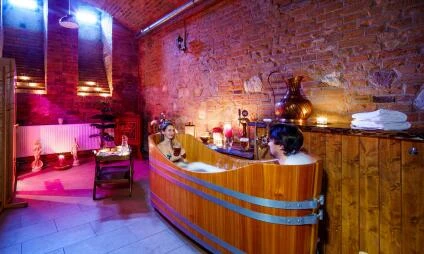 Dřevěný vana s osobou relaxující ve wellness prostoru.